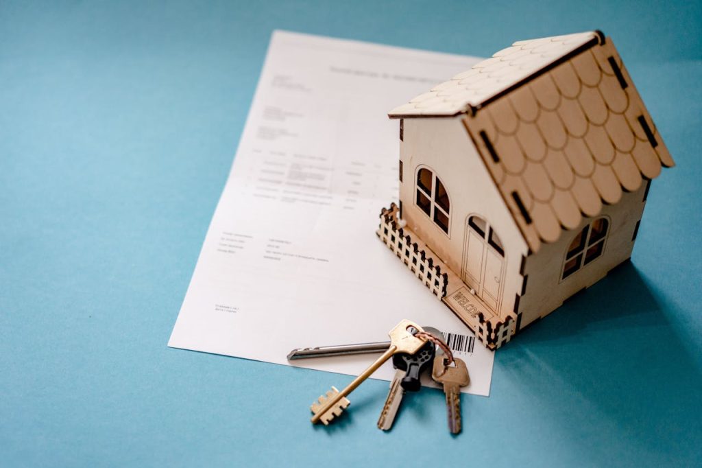 pexels-photo-12955837 Miniature wooden house with keys and contract symbolizing real estate transactions.