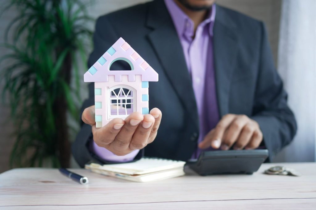 pexels-photo-8732777 Businessman in suit holds model house, calculates real estate investments.
